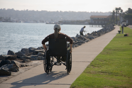 A wheelchair user shown from behind wheeling on a shoreline path