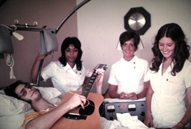 Gary at the age of 18 on his back in a Circle Bed playing his guitar for two nurses and a physical therapist.